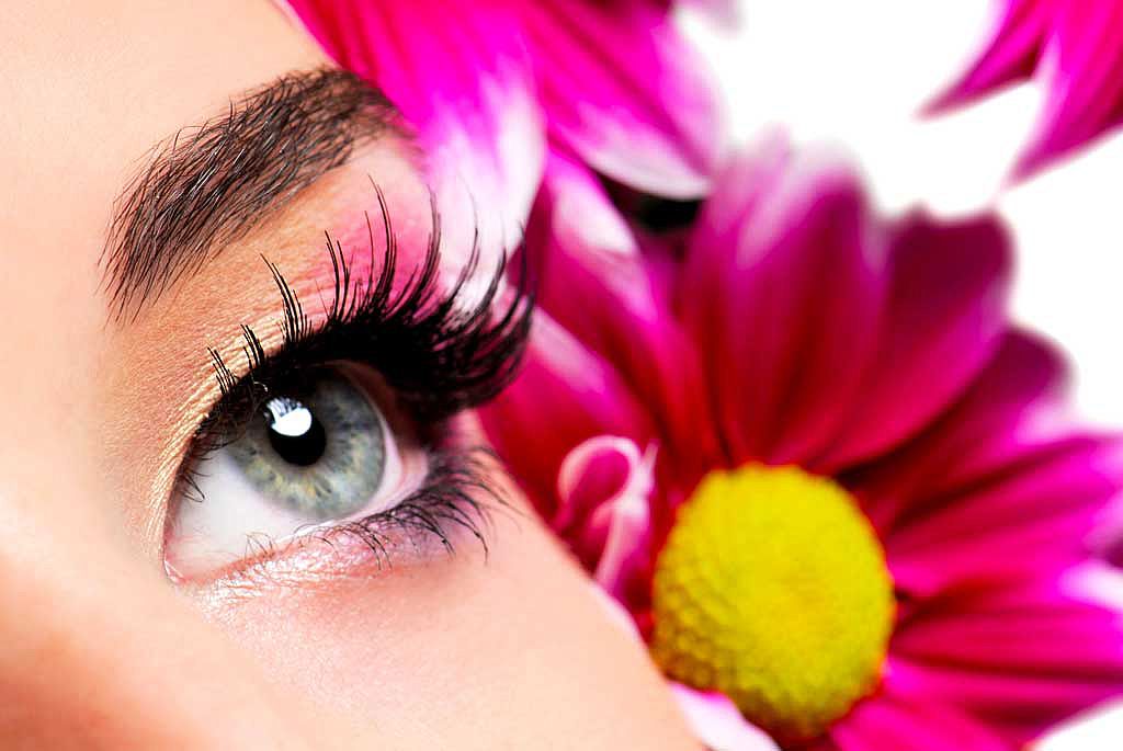 Gros plan sur un oeil de femme maquillé sur fond de fleurs mauves