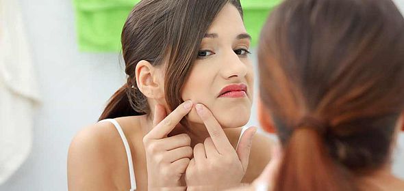 Femme éclatant un bouton d'acné devant son miroir