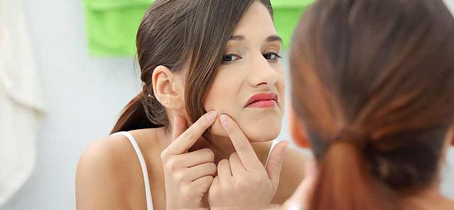 Femme éclatant un bouton d'acné devant son miroir