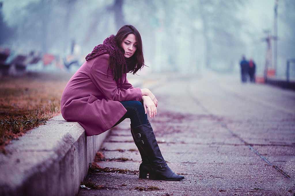 Femme triste assise sur le bord d'un trottoir