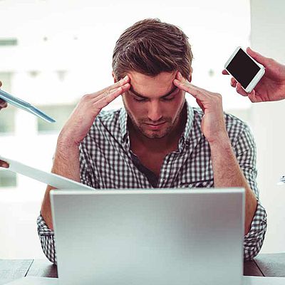 Homme stressé devant son ordinateur sollicité par ses collègues